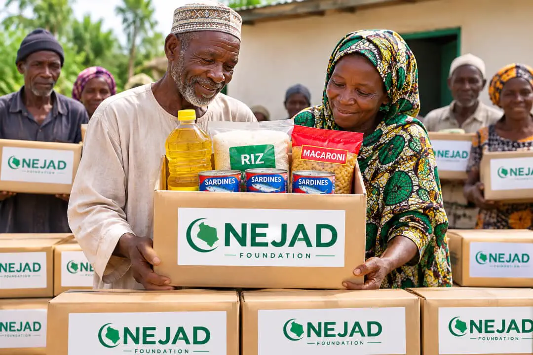 An elderly man and woman hold a NEJAD Foundation food box with rice, oil, pasta and sardines