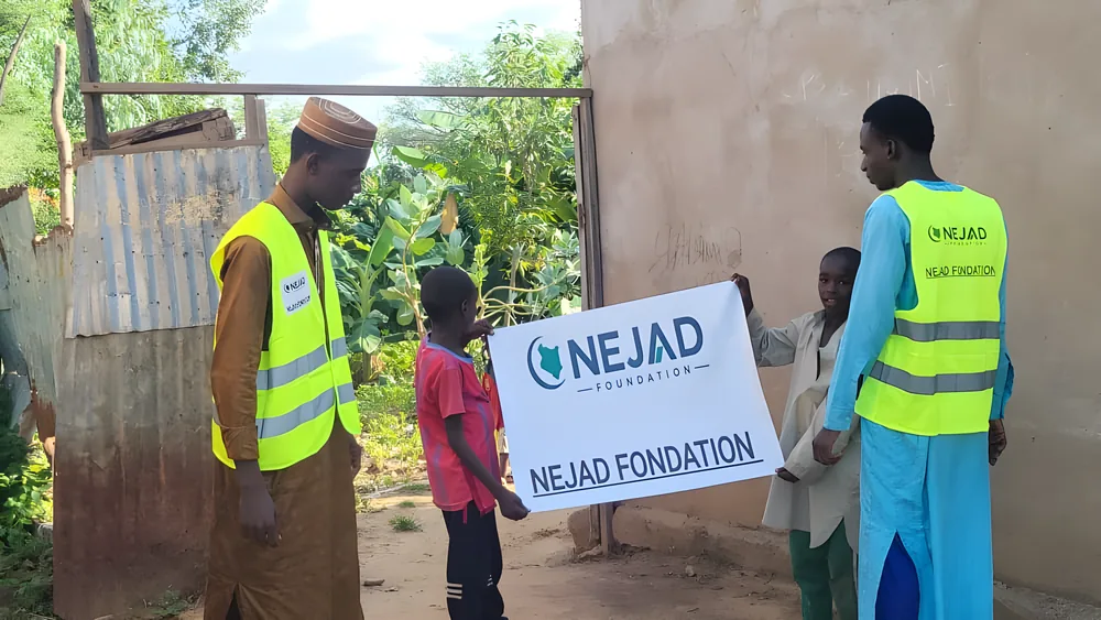 Two NEJAD volunteers and local children holding the foundation's banner